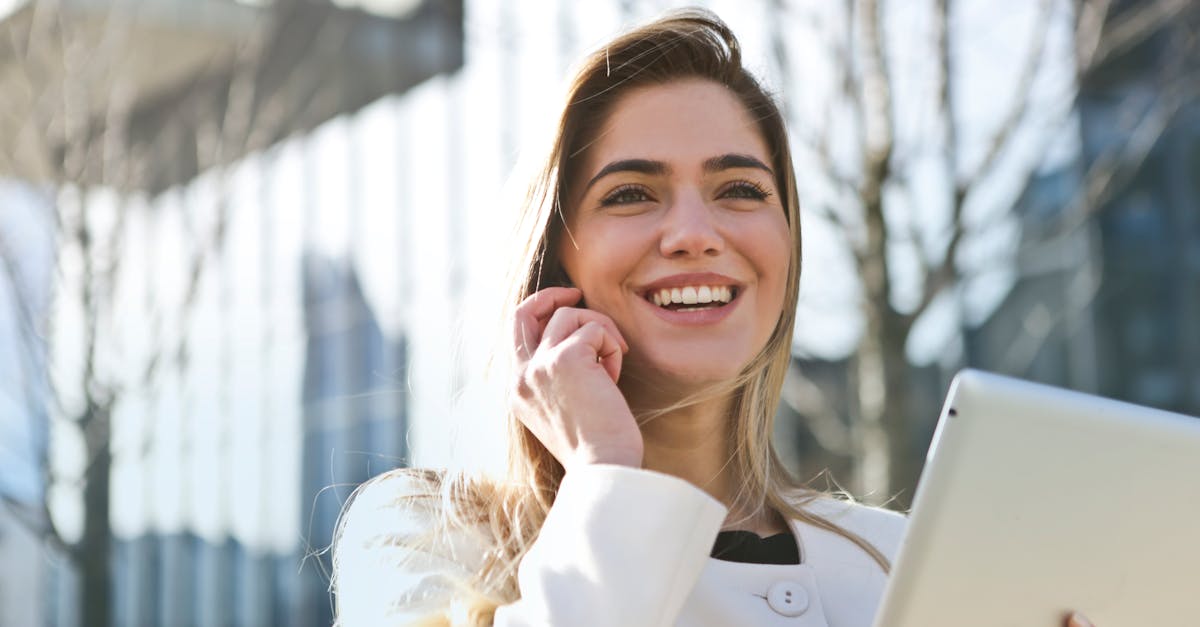 Confident businesswoman using her tablet and phone, smiling outdoors in sunlight.